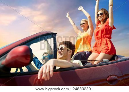 summer holidays, road trip and travel concept - happy friends driving in convertible car and waving hands over sky background