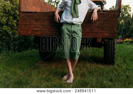 Bare Feet To Stand On The Green Grass. Guy In A White Shirt And With A Green Sweater In Green Shorts