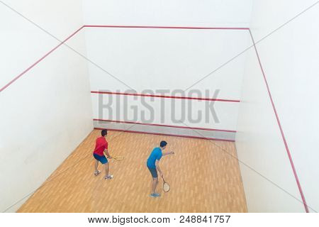 Rear view of two competitive young men with a modern lifestyle playing doubles squash game on a professional court
