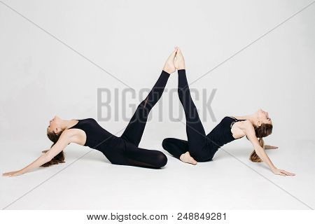 Two Athletics Girls Posing At White Studio, Leaning By Legs Each Other, Lying On Floor In Pose, Look