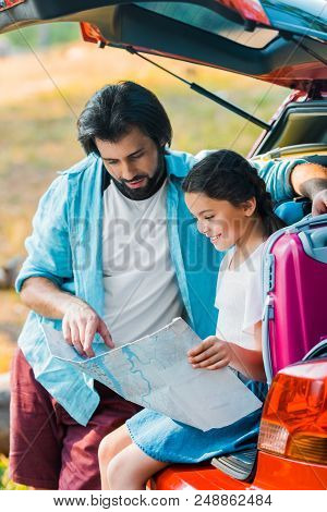 Father And Daughter Looking At Map At Car Trunk