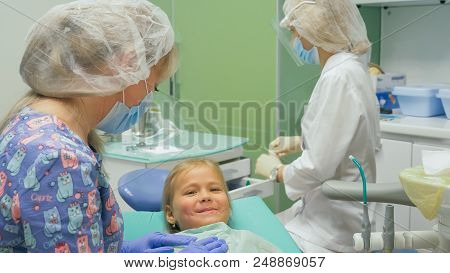 Child With A Mother At A Dentist's Reception. The Girl Lies In The Chair, Behind Her Mother. The Doc