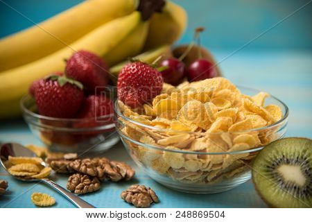 Tasty Cornflakes In Glass Bow With Walnut And Strawberries, Lbananas, Cherry, Kiwi On Blue Backgroun