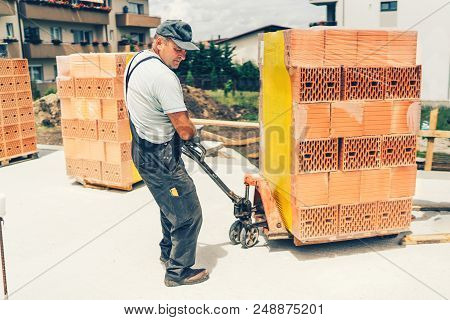 Industrial Worker On Construction Site, Moving Bricks And Working On Building Walls