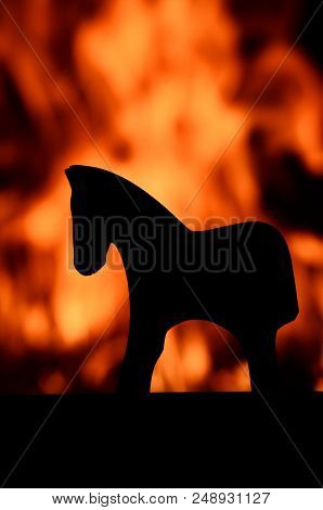 Silhouette Of A Wooden Horse Toy Against A Red, Orange And Yellow Blazing Fire In A House On Fire. B
