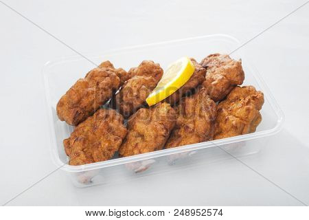 A Plastic Takeaway Container With Onion Bhajis Or Pakora And A Slice Of Lemon.