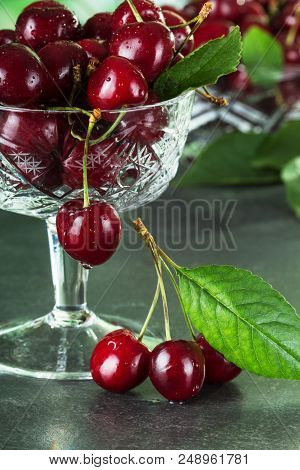 Ripe Moist Cherries In Crystal Vase, On Gray Surface