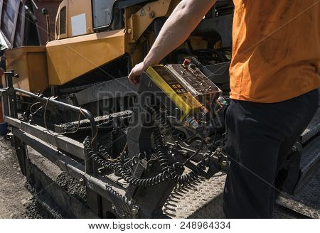 Worker Operating Asphalt Paver Machine During Road Construction And Repairing Works. A Paver Finishe