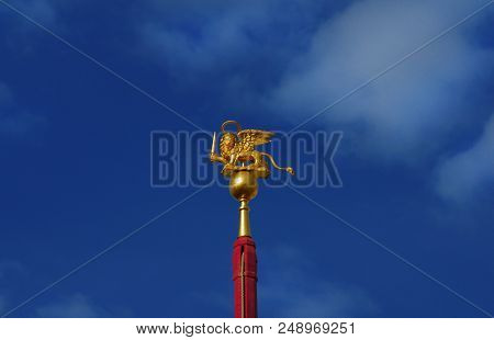 Saint Mark Winged Lion Golden Statuette Wielding A Sword Against Blue Sky, A Symbol Of The Old Venic