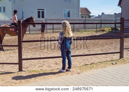 Back View Of Kid Looking At Mother Riding Horse At Farm