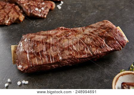 Hot Grilled Whole Flank Steak on Black Stone Background. Fresh Juicy Medium Rare Beef Grillsteak. Barbecue Meat Close Up