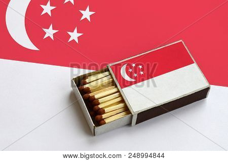 Singapore Flag  Is Shown In An Open Matchbox, Which Is Filled With Matches And Lies On A Large Flag.