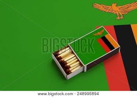 Zambia Flag  Is Shown In An Open Matchbox, Which Is Filled With Matches And Lies On A Large Flag.
