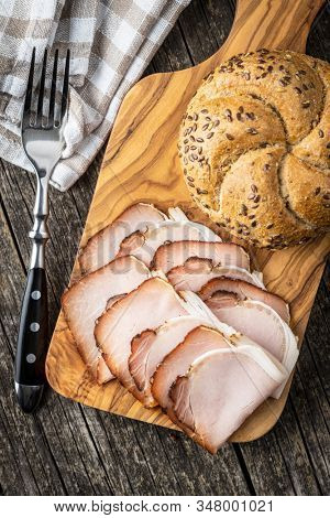 Sliced smoked ham. Tasty pork meat and bun on wooden cutting board. Top view.