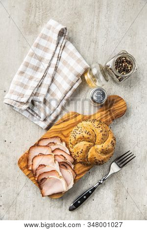 Sliced smoked ham. Tasty pork meat and bun on wooden cutting board. Top view.