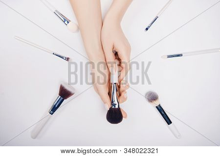Girl Hand Hold White Brushes Makeup On White Background. Top View Flat Lay