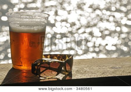 Glas Bier und Sonnenbrillen sitzen auf der Schiene des ein Deck mit Blick auf Wasser