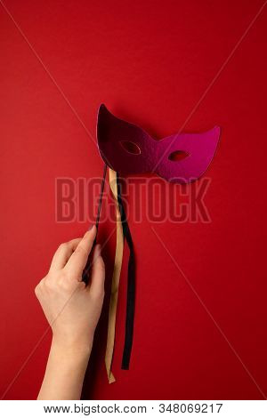 Woman Hand Holding  Festive, Colorful Mardi Gras Or Carnivale Mask Over Red Background. Party Invita