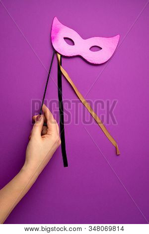 Woman Hand Holding  Festive, Colorful Mardi Gras Or Carnivale Mask Over Purple Background. Party Inv