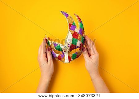 Woman Hand Holding  Festive, Colorful Mardi Gras Or Carnivale Mask Over Yellow Background. Party Inv