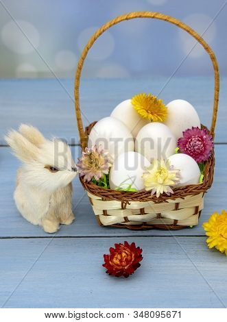 The Easter Bunny Sits Next To A Basket Full Of Eggs, Decorated With Dried Flowers.