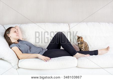 Beautiful Cheerful Woman Lying On Sofa With Bengal Cat.