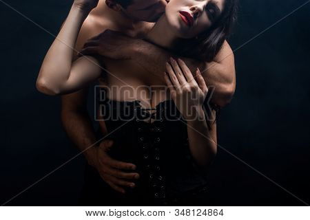 Shirtless Man Hugging And Kissing Sexy Girlfriend In Corset Isolated On Black