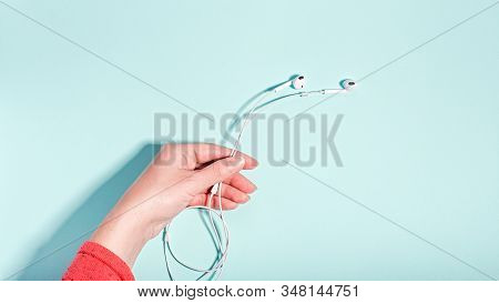 White Earphones In Female Hand On Pastel Background, Copy Space. Modern Technology Flat Lay With Cor
