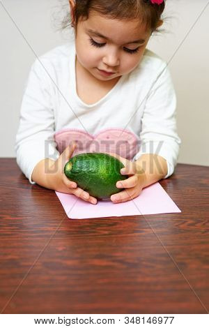 Little Cute Smiling Black Hair Girl Holding Green Avocado. Healthy Food For Children Concept.