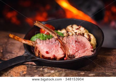 Two Juicy Pieces Of Rack Of Lamb In A Pan With Tomato And Basil On A Background Of Fire From The Ove