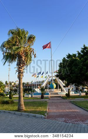Turkey, Hatay - August 24, 2019: The Monument With Waving Flag In Iskenderun With Palm Trees