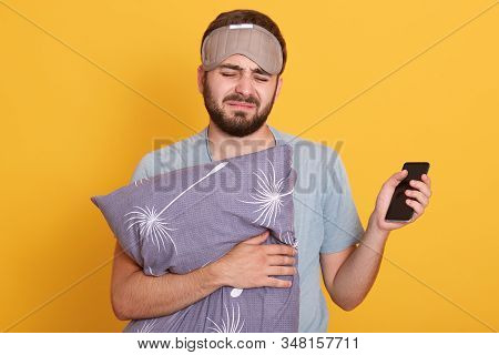 Horizontal Indoor Shot Of Sleepy Miserable Man Wearing Sleeping Mask And T Shirt, Holding Pilow And 