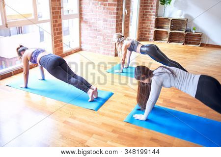 Young beautiful group of sportswomen smiling happy practicing yoga doing plank pose at gym