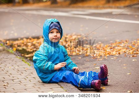 Happy Child In Waterproof Coat And Rainboots Outdoors In Autumn Season.