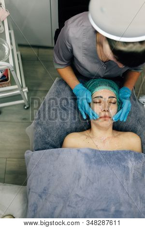 Young Woman Receives Cosmetic Procedure To Rejuvenate Her Face In A Beauty Salon, Photo Above