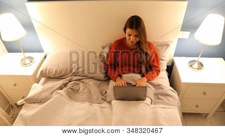 Young Beautiful Woman Is Using Laptop Computer On Double Bed At The Night Time