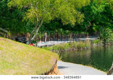 Teenage Girl Walking Away Along A Path Around Lake At Mclaren Falls Park, Tauranga New Zealand