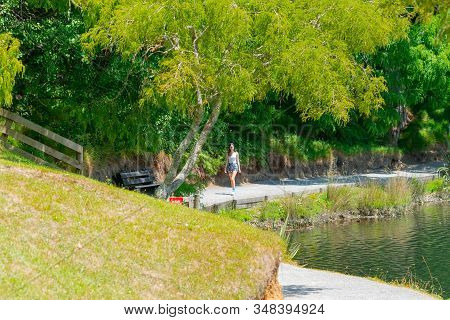 Teenage Girl Walking Towards In Distance Along A Path Around Lake At Mclaren Falls Park, Tauranga Ne