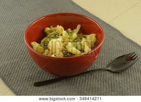 Roasted Cauliflower With Pepitas In Red Bowl With Black Spork On Burlap Table Runner