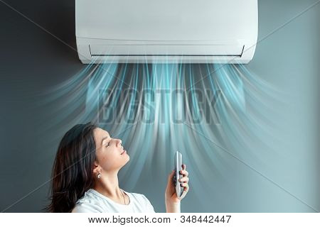 A Beautiful Girl Stands Under Air Conditioning And A Stream Of Fresh Cold Air Against A Gray Wall. T