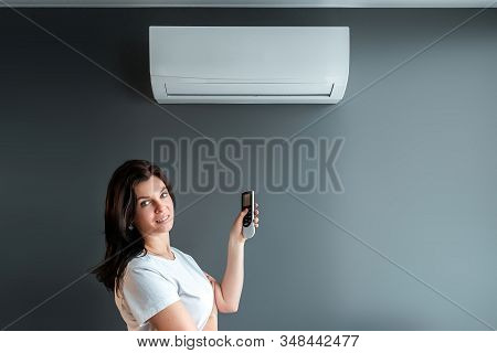 A Beautiful Girl Stands Under Air Conditioning And A Stream Of Fresh Cold Air Against A Gray Wall. T