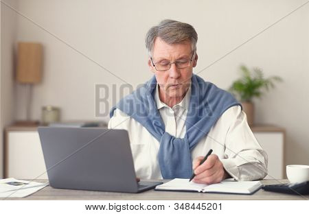 Elderly Businessman Working On Laptop Taking Notes Sitting In Modern Office. No Ageism Concept. Sele