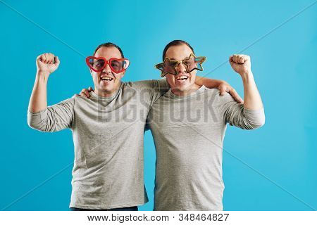Caucasian Twin Brothers Wearing Funny Eyeglasses Ready For Prty Looking At Camera, Bright Blue Backg