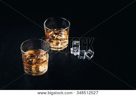 Whisky, Whiskey, Bourbon Or Cognac With Ice Cudes On Black Stone Table