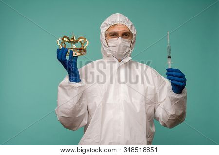 A Male Doctor In Protective Overalls And A Mask Holds An Syringe With A Vaccine And Crown In His Han