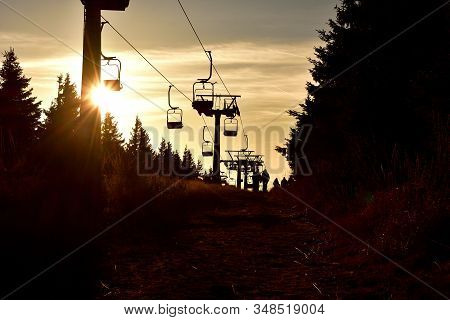 People Walks Under Ski Chair Lift In The Mountains At Sunset.