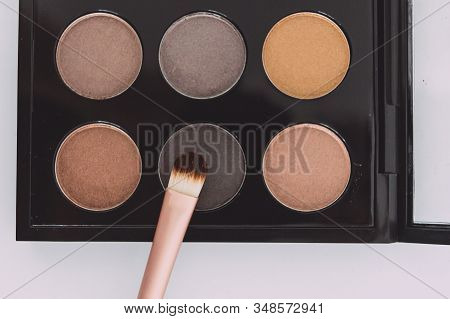Close-up Of Brush On Top Of Eyeshadow Palette With Trendy Nudes And Bronzy Tones