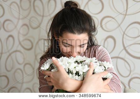 Girl Sniffs A Bouquet Of White Flowers. Brunette Hugs Sniffs A Bouquet Of Delicate Flowers From Her 