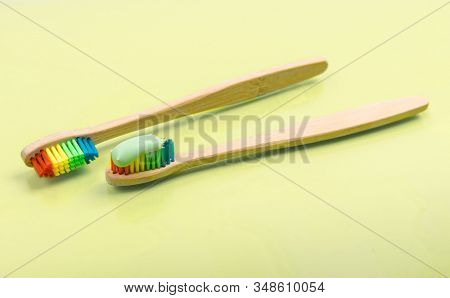 Bamboo toothbrush with eco green toothpaste on pastel background. Pair of multi-colored wooden tooth brushes