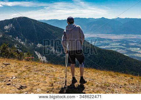 Hiker Man With Injured Knee Holding Medicine Crutch. Young Man Enjoying The Scenic View To Valley Fr